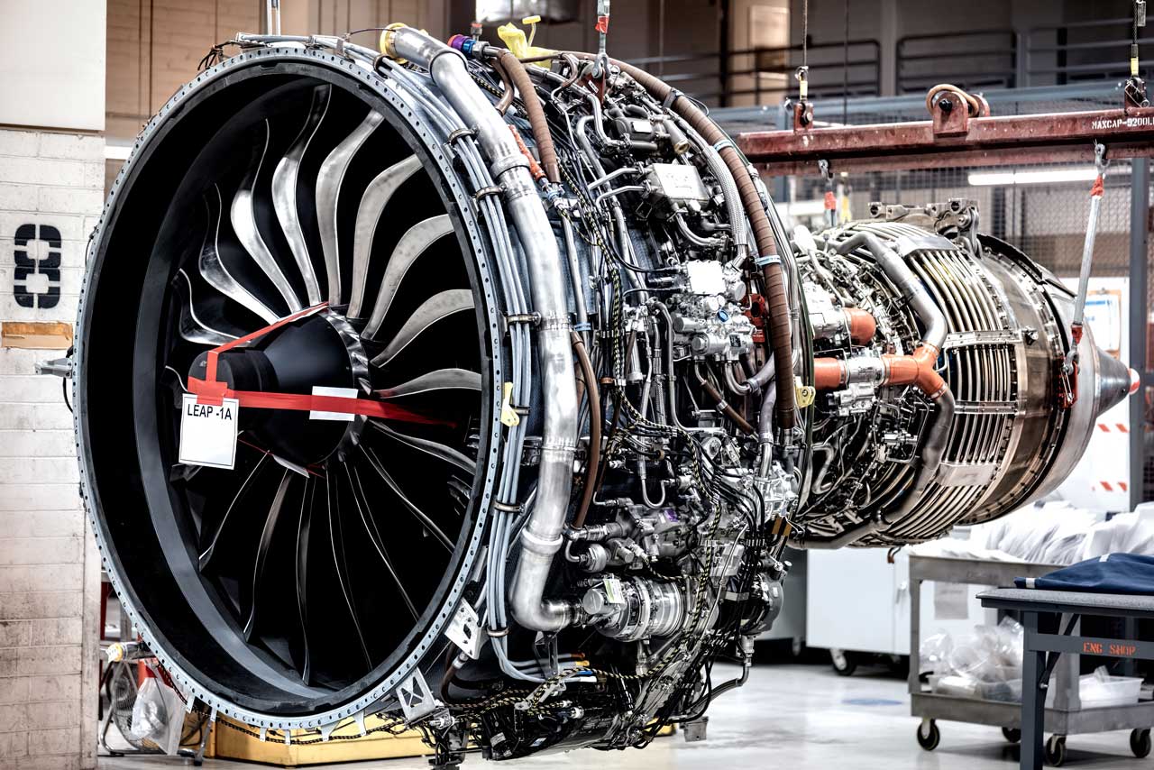 A complex, uncovered jet engine is hoisted off the ground.