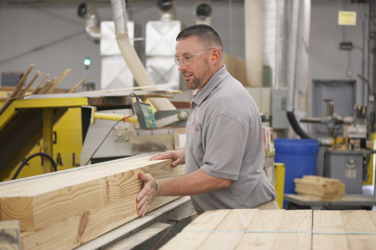 man-pushing-wood-through-planer A man guides a large piece of timber across an industrial planer.