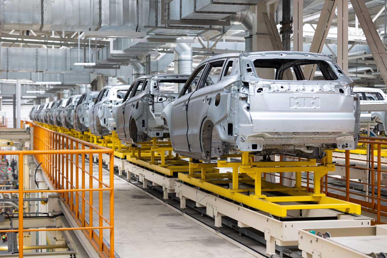 photo-of-automobile-production-line-welding Incomplete, bare car bodies mounted on steel racks inside an assembly plant.