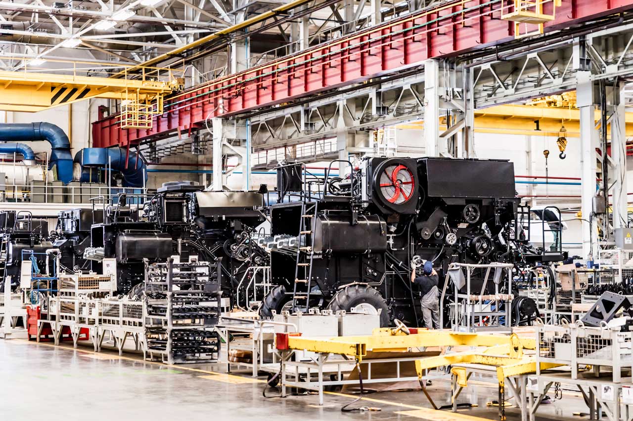 A very busy photo that shows a combine harvester being assembled and parts and packaging strewn about in a manufacturing plant.