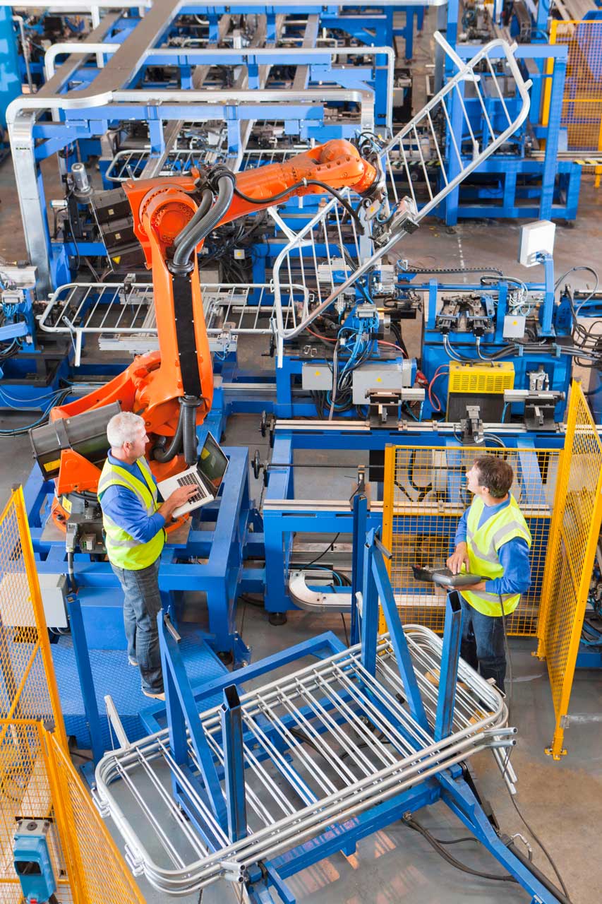 Workers watch robotic equipment lift product off a custom steel rack